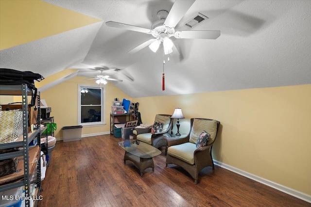 living area with dark wood-type flooring, vaulted ceiling, a textured ceiling, and ceiling fan