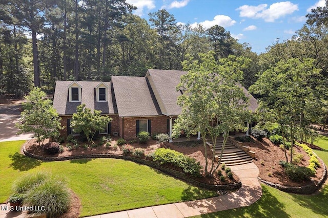 tudor home featuring brick siding, roof with shingles, a front lawn, and stairs