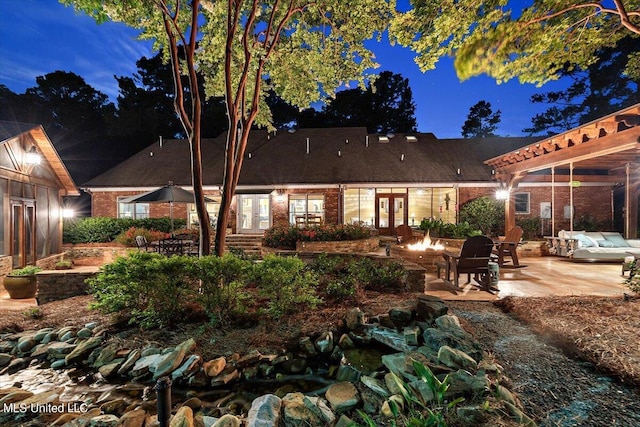 back of house at twilight with a patio area, a fire pit, french doors, and brick siding
