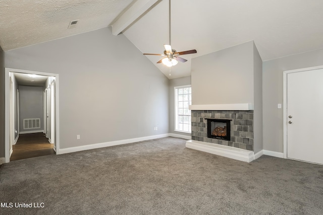 unfurnished living room featuring ceiling fan, a textured ceiling, vaulted ceiling with beams, a fireplace, and dark colored carpet