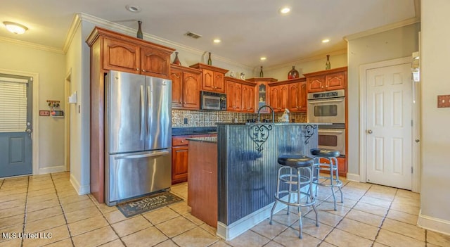 kitchen featuring light tile patterned floors, a breakfast bar area, a kitchen island with sink, crown molding, and appliances with stainless steel finishes