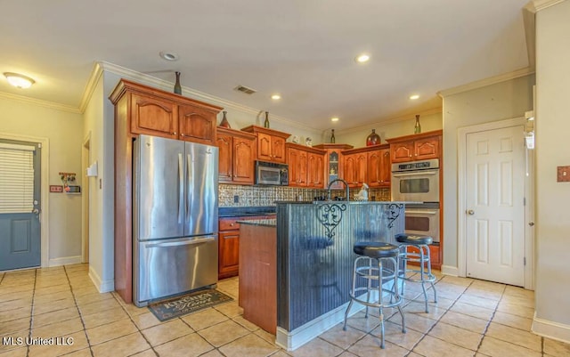 kitchen with stainless steel appliances, a kitchen breakfast bar, light tile patterned floors, an island with sink, and crown molding