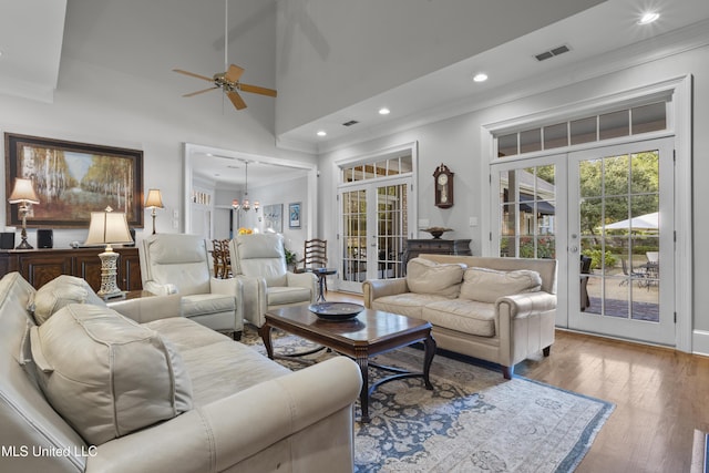 living room with a high ceiling, wood-type flooring, ornamental molding, ceiling fan with notable chandelier, and french doors