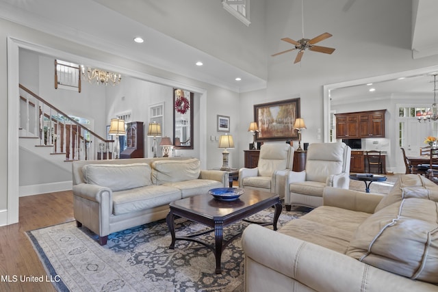 living room featuring ceiling fan with notable chandelier, ornamental molding, light hardwood / wood-style floors, and a high ceiling