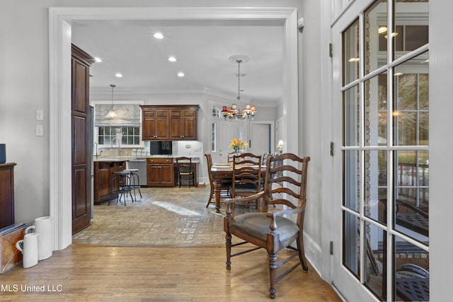 dining space featuring crown molding, a chandelier, sink, and light wood-type flooring