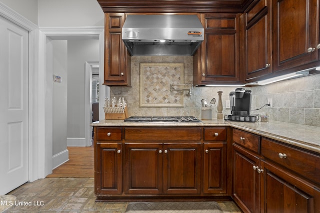 kitchen featuring stainless steel gas stovetop, light stone countertops, exhaust hood, and backsplash