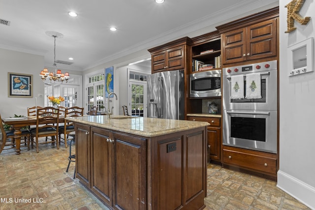 kitchen with light stone counters, ornamental molding, stainless steel appliances, and a kitchen island with sink