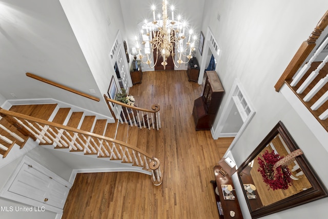 stairs with hardwood / wood-style flooring, a towering ceiling, and an inviting chandelier