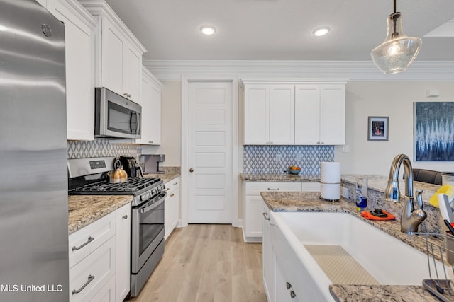 kitchen featuring stainless steel appliances, ornamental molding, decorative light fixtures, white cabinetry, and light hardwood / wood-style floors