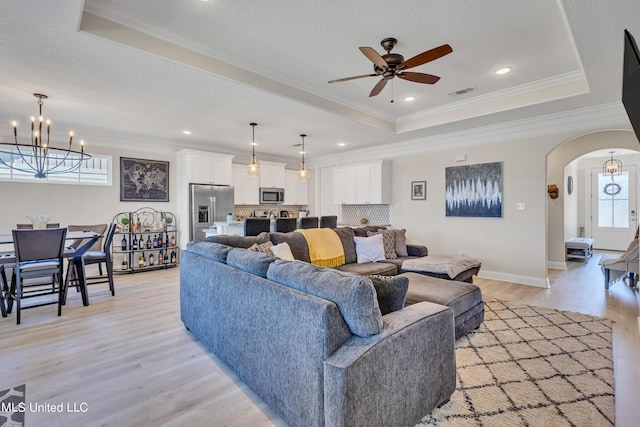 living room with a wealth of natural light, crown molding, light hardwood / wood-style flooring, and a tray ceiling