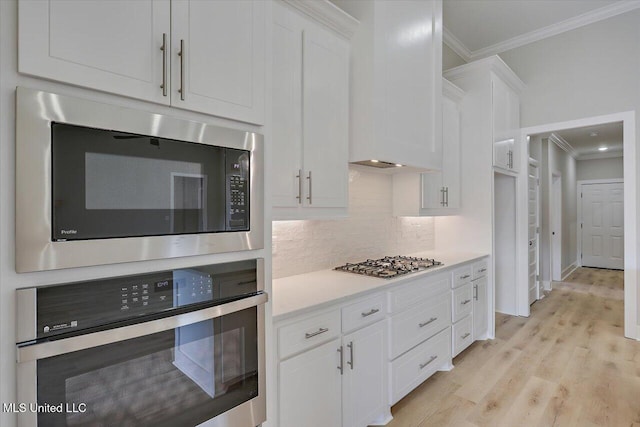 kitchen with ornamental molding, appliances with stainless steel finishes, backsplash, and white cabinets