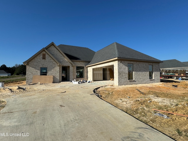 view of front of property featuring a shingled roof, brick siding, driveway, and a garage