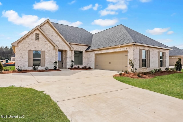 french country inspired facade with roof with shingles, concrete driveway, a front lawn, and a garage