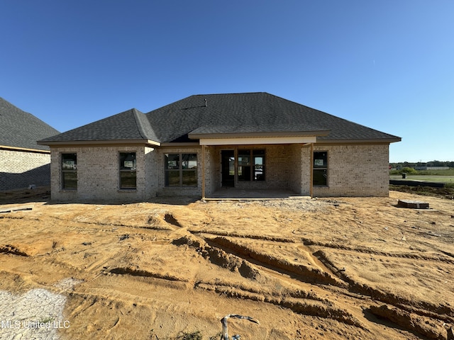 back of house with a shingled roof, brick siding, and a patio