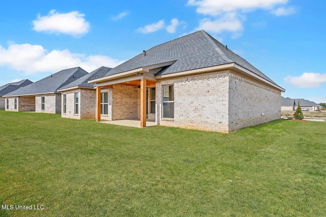 back of property with roof with shingles, a lawn, a patio area, and brick siding