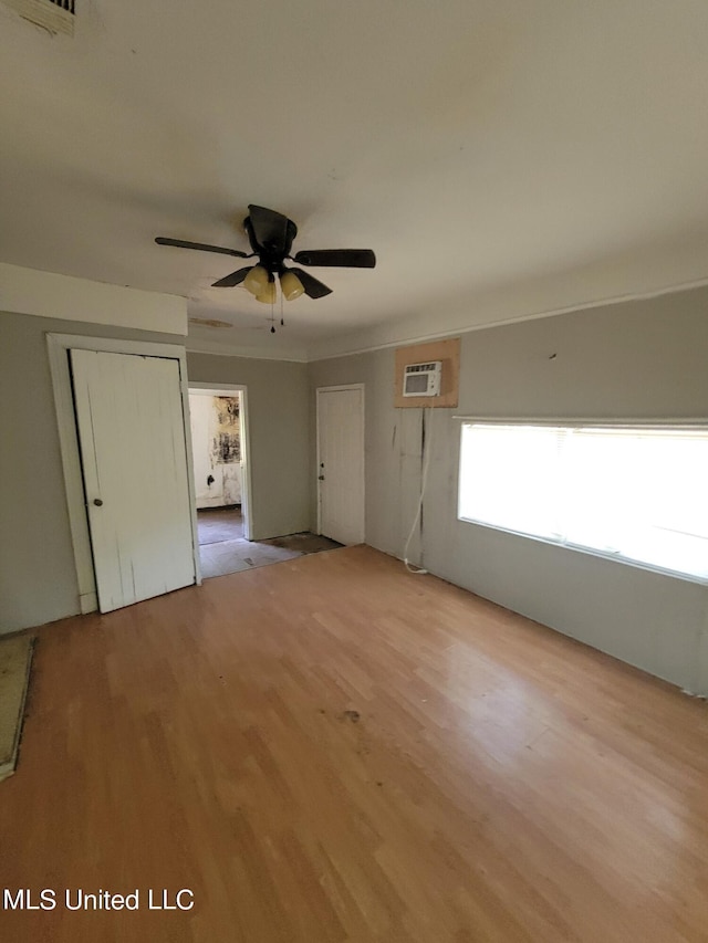 empty room featuring light wood-style floors, a ceiling fan, an AC wall unit, and visible vents