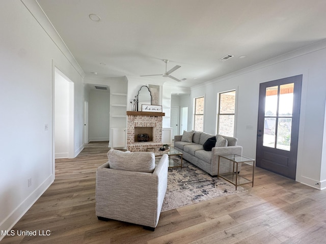 living room featuring ceiling fan, ornamental molding, wood-type flooring, and a brick fireplace