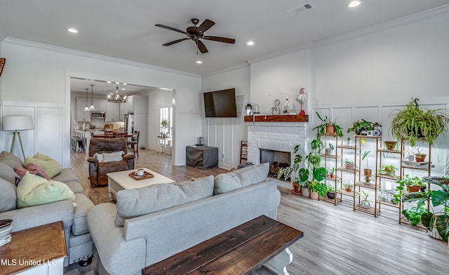 living room featuring crown molding, ceiling fan, light hardwood / wood-style floors, and a brick fireplace