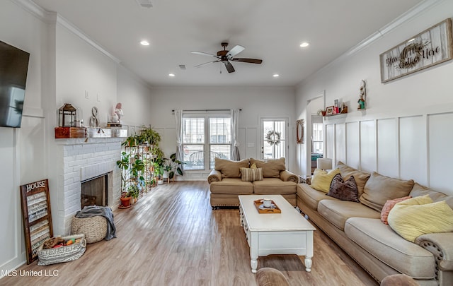 living room featuring a fireplace, ornamental molding, ceiling fan, and light wood-type flooring