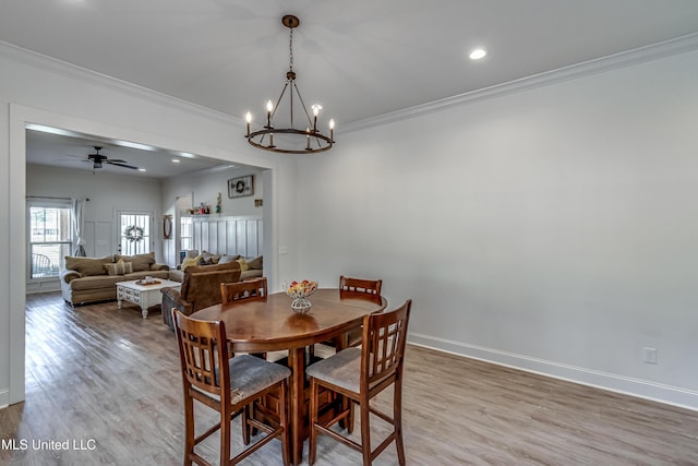 dining space with crown molding, wood-type flooring, and ceiling fan with notable chandelier