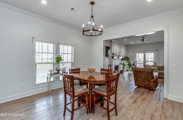 dining room featuring crown molding, a fireplace, ceiling fan with notable chandelier, and light hardwood / wood-style flooring