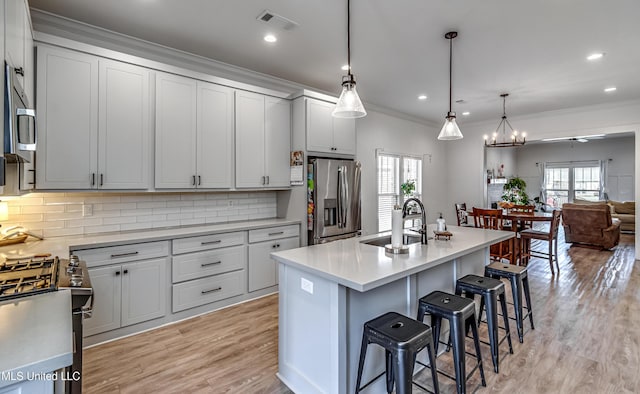 kitchen featuring decorative light fixtures, sink, a kitchen bar, stainless steel appliances, and a center island with sink