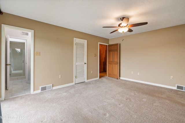 unfurnished bedroom with ensuite bathroom, light colored carpet, a textured ceiling, a closet, and ceiling fan