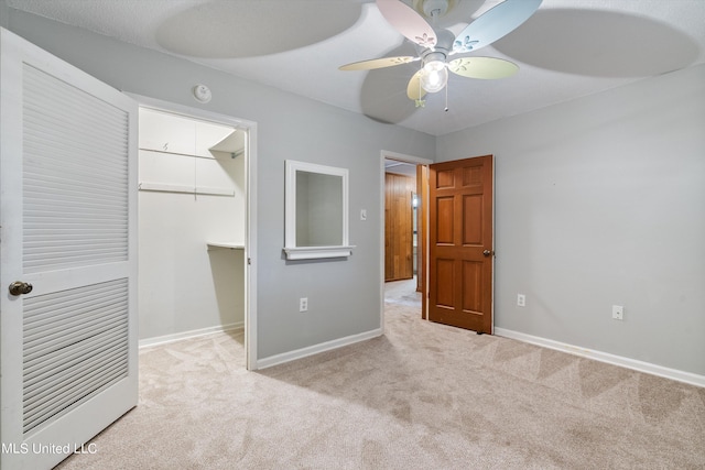 unfurnished bedroom with a walk in closet, light colored carpet, a closet, and ceiling fan