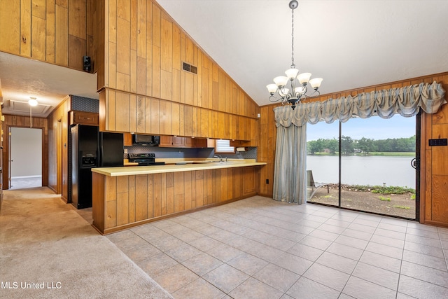 kitchen with wood walls, a water view, an inviting chandelier, kitchen peninsula, and black appliances