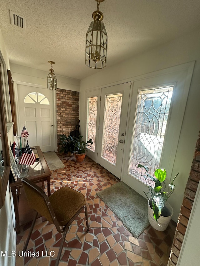 entryway with an inviting chandelier, visible vents, and a textured ceiling