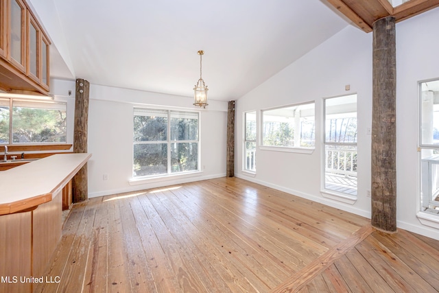 unfurnished dining area with beam ceiling, high vaulted ceiling, a healthy amount of sunlight, and light hardwood / wood-style floors