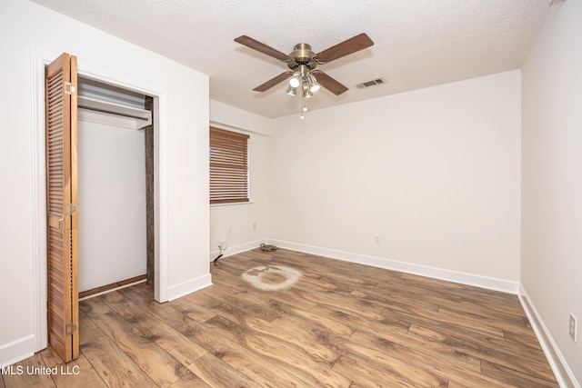 unfurnished bedroom featuring wood-type flooring, a textured ceiling, a closet, and ceiling fan