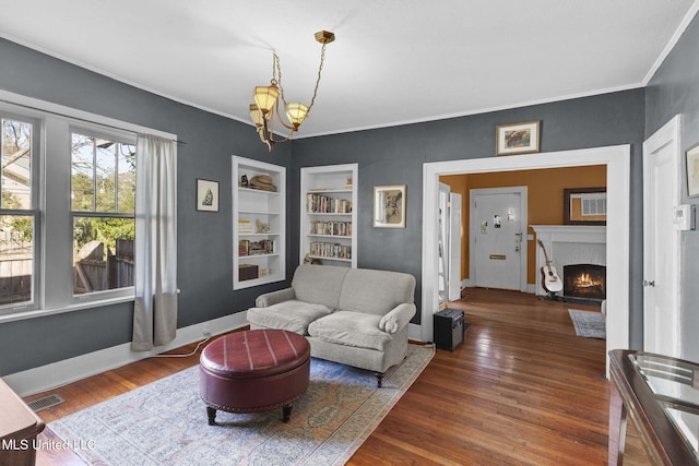 living room featuring a chandelier, built in shelves, dark hardwood / wood-style floors, and a fireplace