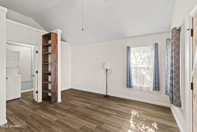 unfurnished bedroom with dark hardwood / wood-style floors, lofted ceiling, and stacked washer and clothes dryer