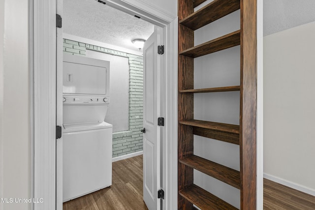 washroom featuring a textured ceiling, dark hardwood / wood-style flooring, and stacked washer and dryer