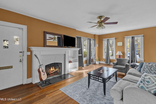 living room with ceiling fan, a healthy amount of sunlight, wood-type flooring, and a brick fireplace