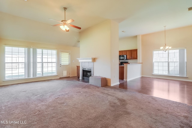 unfurnished living room featuring carpet floors, a tiled fireplace, high vaulted ceiling, and a healthy amount of sunlight