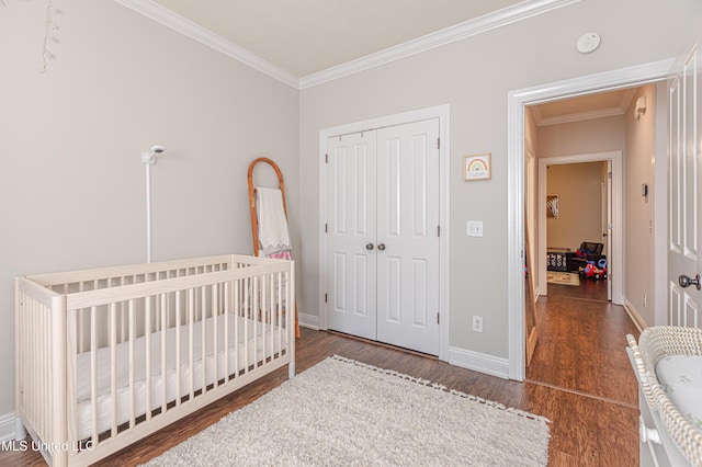 bedroom with crown molding, dark hardwood / wood-style flooring, a closet, and a crib