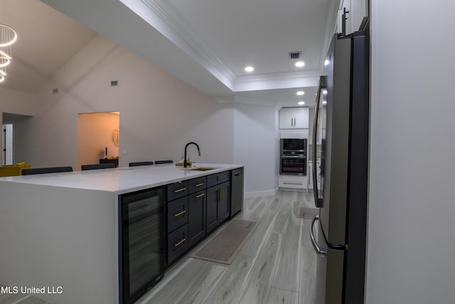 kitchen with beverage cooler, freestanding refrigerator, light countertops, light wood-type flooring, and a sink