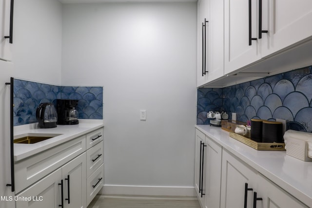 kitchen with light countertops, decorative backsplash, white cabinets, light wood-type flooring, and baseboards