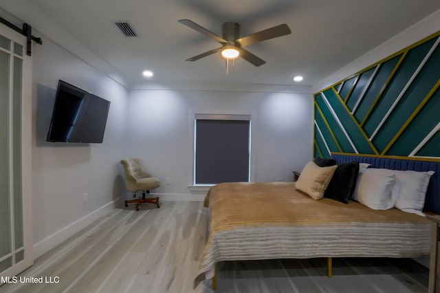 bedroom with a barn door, recessed lighting, wood finished floors, visible vents, and baseboards