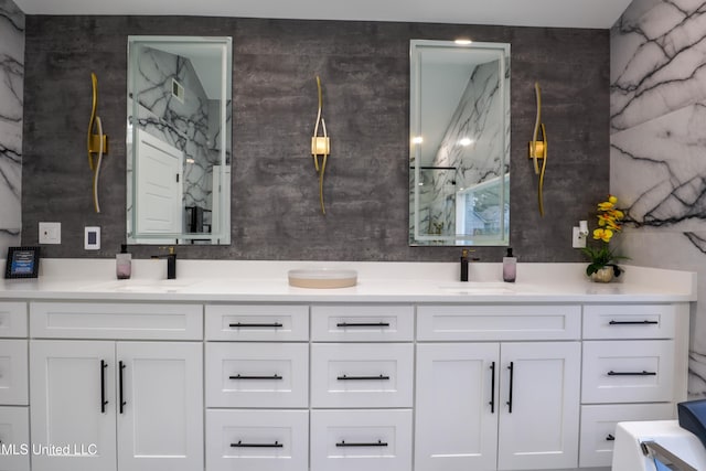 bathroom with a sink, a marble finish shower, and double vanity