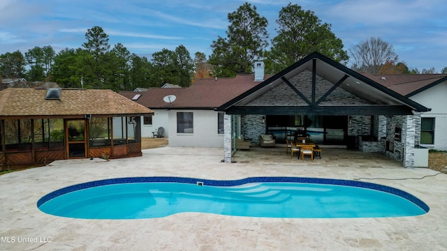 rear view of property featuring a patio, a shingled roof, a sunroom, an outdoor pool, and a chimney