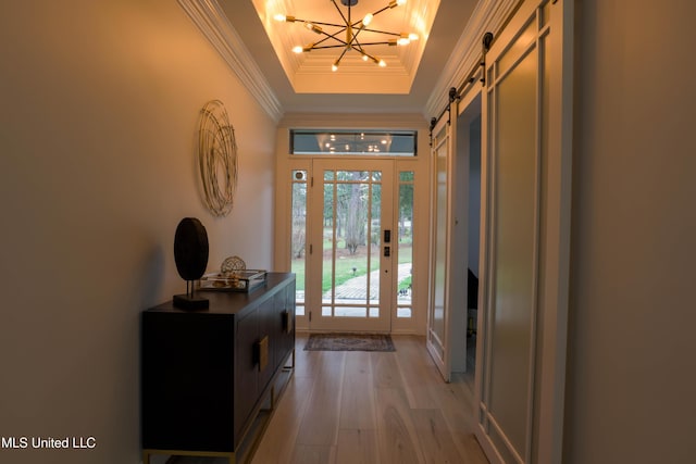 entryway featuring a barn door, a notable chandelier, light wood-style floors, ornamental molding, and a raised ceiling