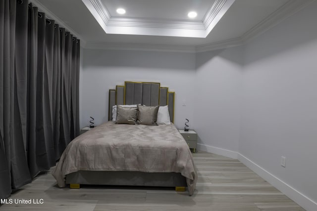 bedroom featuring light wood-style floors, a raised ceiling, crown molding, and baseboards