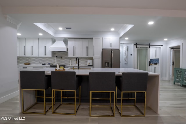 kitchen featuring a barn door, stainless steel fridge with ice dispenser, custom exhaust hood, light countertops, and crown molding