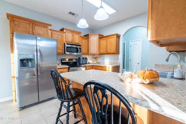 kitchen with hanging light fixtures, a breakfast bar area, appliances with stainless steel finishes, light tile patterned floors, and sink