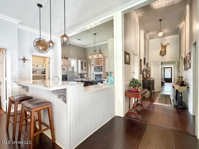 kitchen with hanging light fixtures, dark hardwood / wood-style flooring, appliances with stainless steel finishes, a kitchen breakfast bar, and crown molding