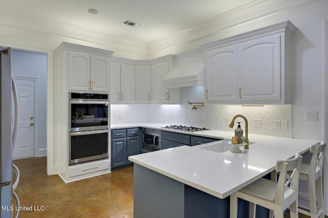 kitchen with wall chimney exhaust hood, white cabinetry, appliances with stainless steel finishes, a kitchen breakfast bar, and backsplash