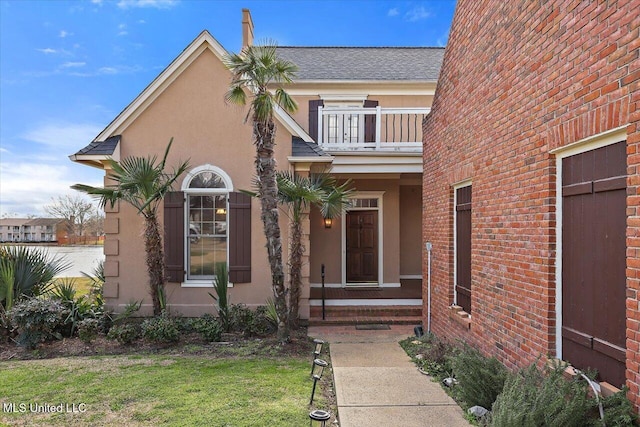 view of exterior entry featuring stucco siding, a balcony, and roof with shingles